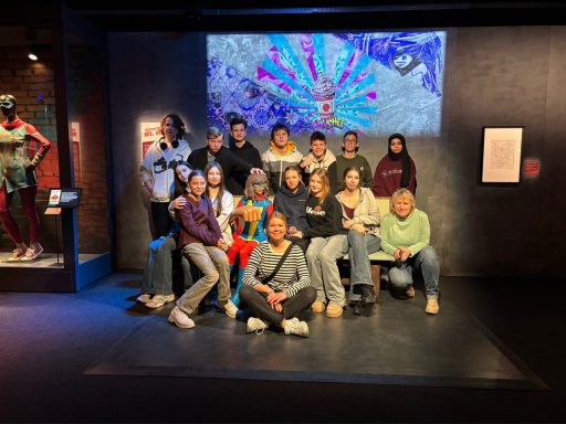 Gruppe von Personen in einem Ausstellungsraum, mit buntem Hintergrund und interaktiven Exponaten.