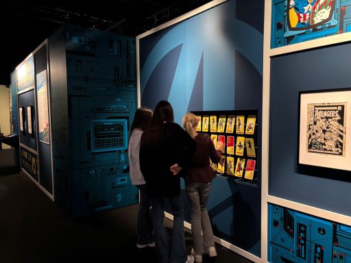 Besucher betrachten Ausstellungsstücke in einem Museum, umgeben von bunten Wandgestaltungen.